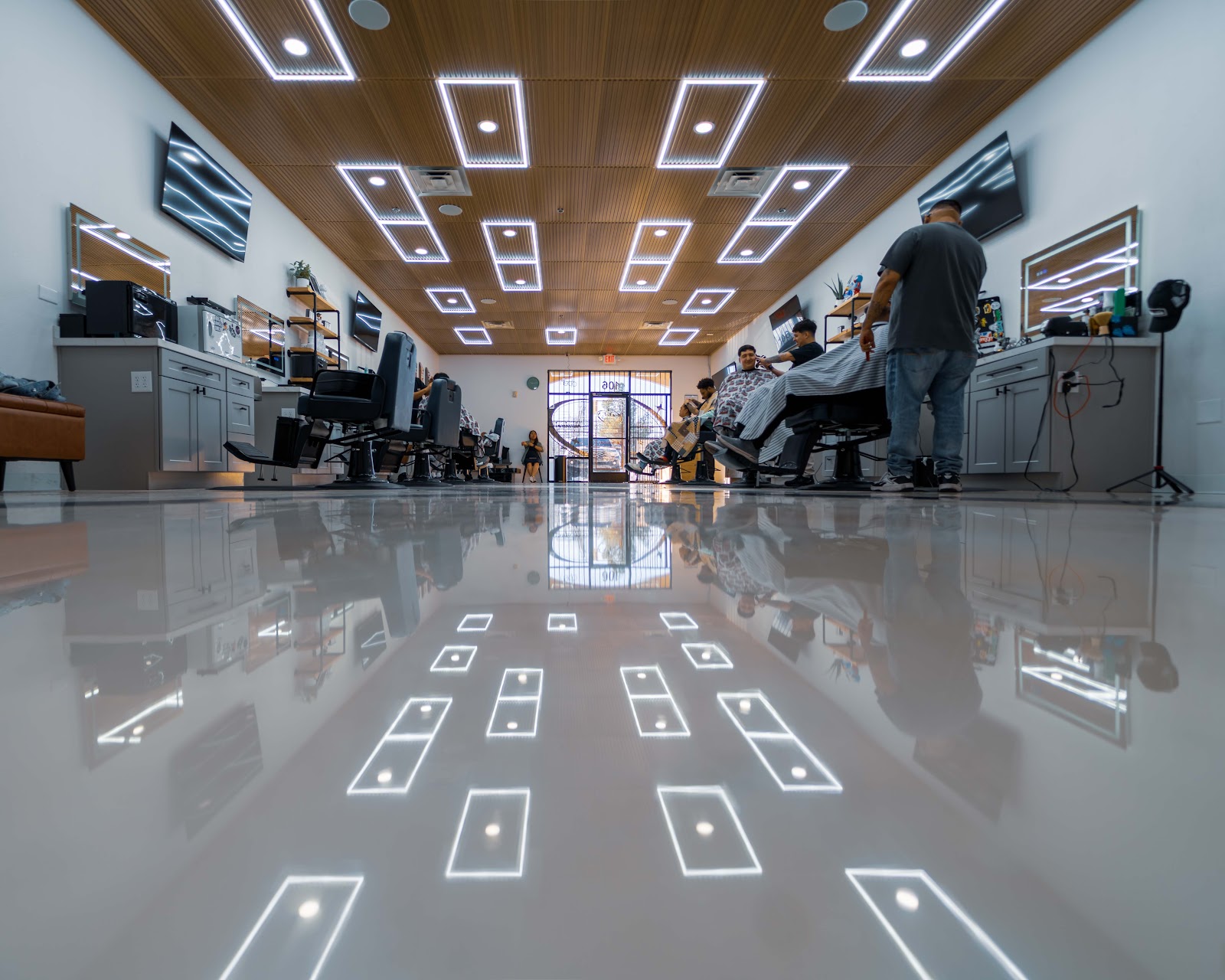 Wide symmetrical view of barbershop interior with reflective floor, geometric lighting, and barbers working