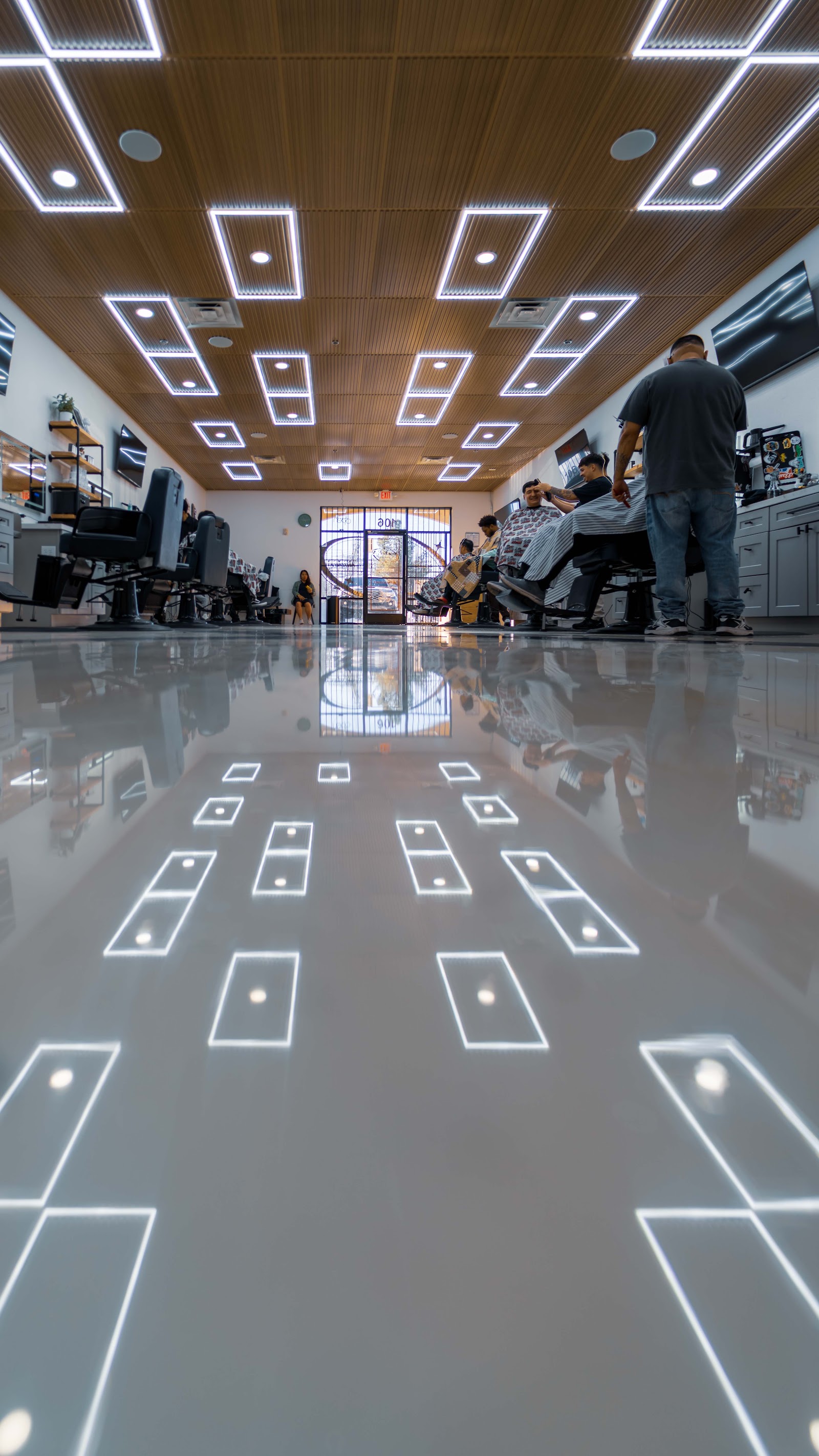 Low-angle view of modern barbershop interior with glossy floor, geometric ceiling lights, and barbers at work